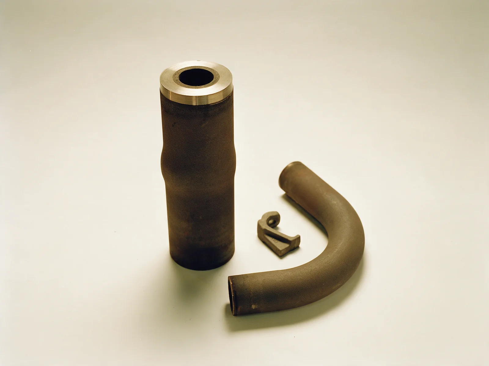A sectioned centrifugally cast reformer tube beside a bent pigtail and a small fitting