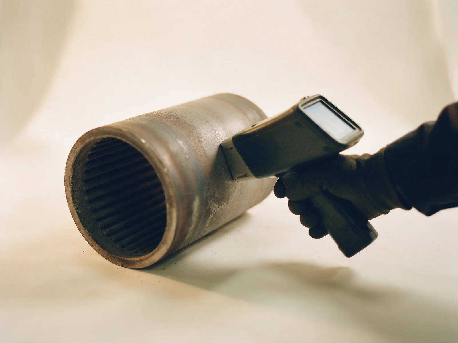 A handheld XRF analyser reading the wall of a cast alloy tube